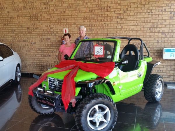 Couple standing behind green off-road buggy with red bow