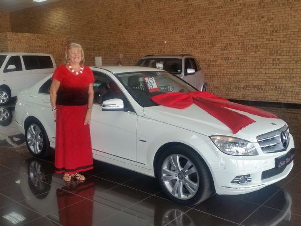 Woman standing beside white Mercedes with red gift bow