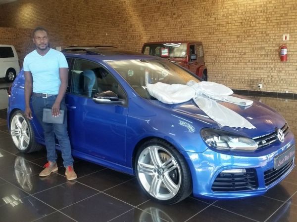 Man standing beside blue Volkswagen with large white bow