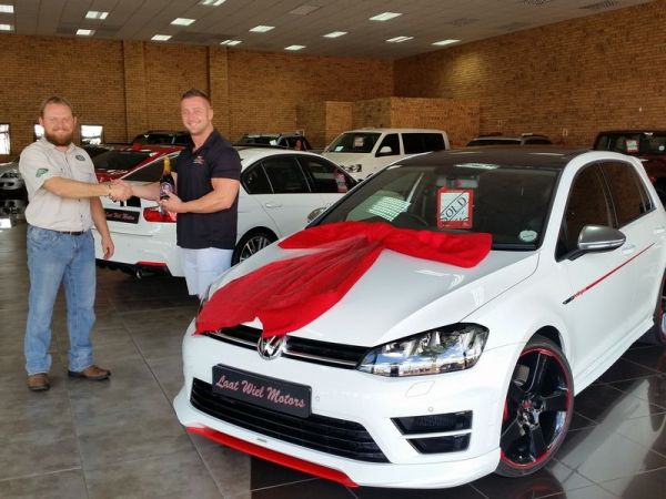 Men shake hands beside ribboned white Volkswagen in showroom