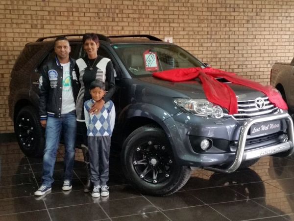 Family posing beside ribbon-wrapped Toyota SUV at dealership