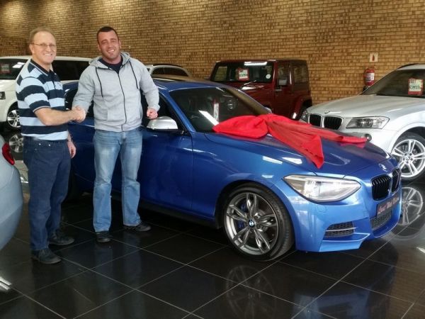 Two men beside blue BMW with red unveiling cloth