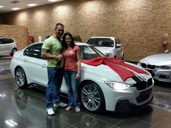 Couple posing beside white BMW with red bow